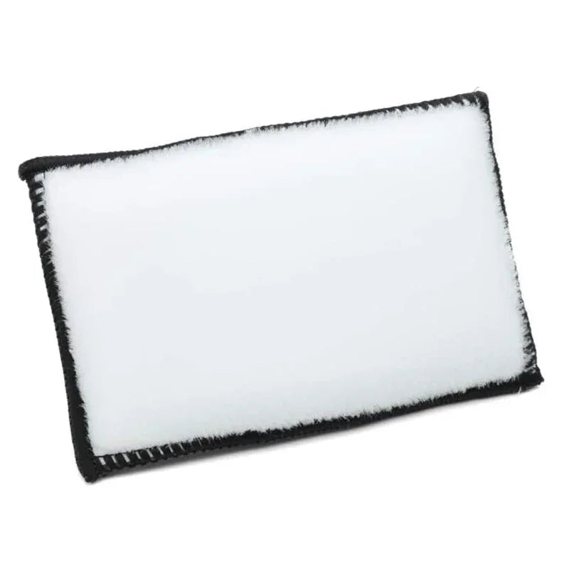 A rectangular white microfiber scrub sponge with a black edge.