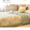 A beige quilted bedspread with gold leaf embroidery is displayed on a bed, emphasizing breathable and durable fabric features
