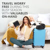 A smiling woman wearing a cream sweater is sitting on a bed with a blue suitcase and a yellow blanket.