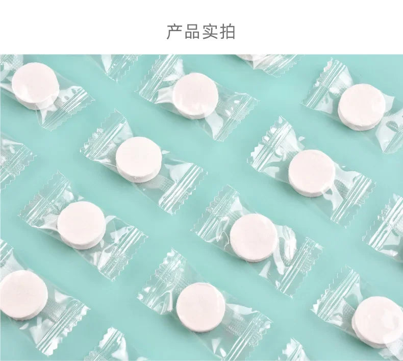 A flat lay of several clear plastic packets containing white portable compressed cleansing towels on a light blue surface.