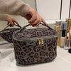 A close-up of a dark gray leopard print cosmetic bag being held by a hand.