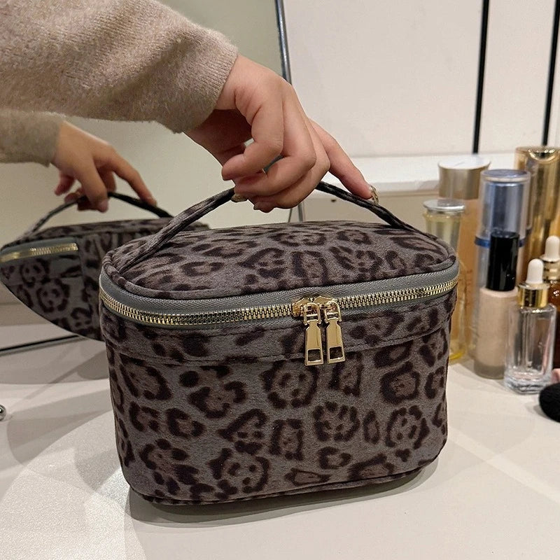 A close-up of a dark gray leopard print cosmetic bag being held by a hand.