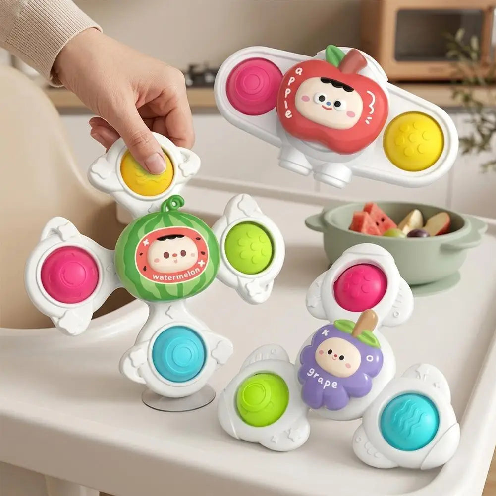 A collection of baby suction cup spinner toys featuring various fruits like apple, watermelon, and grape in pink, green, and 