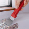 A hand holds a red kitchen cleaning brush set with a metal scraper tool resting on a light surface.