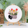 Embroidery kit featuring pre-printed floral and cat designs on white fabric displayed on a wooden easel.