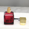A glass perfume bottle with a red liquid and a gold sprayer, next to its empty cap.
