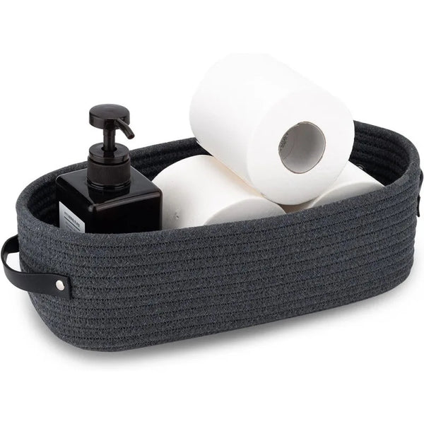 A dark gray woven cotton rope storage basket filled with white toilet paper rolls and a black dispenser.