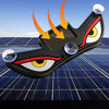 A black, eye-shaped solar-powered LED car window decal is shown resting on a blue solar panel surface.