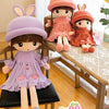 A plush doll of a girl with long brown hair and pink clothing sitting on a wooden table.