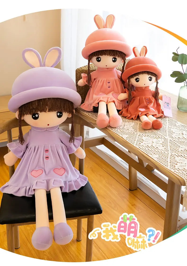 A plush doll of a girl with long brown hair and pink clothing sitting on a wooden table.