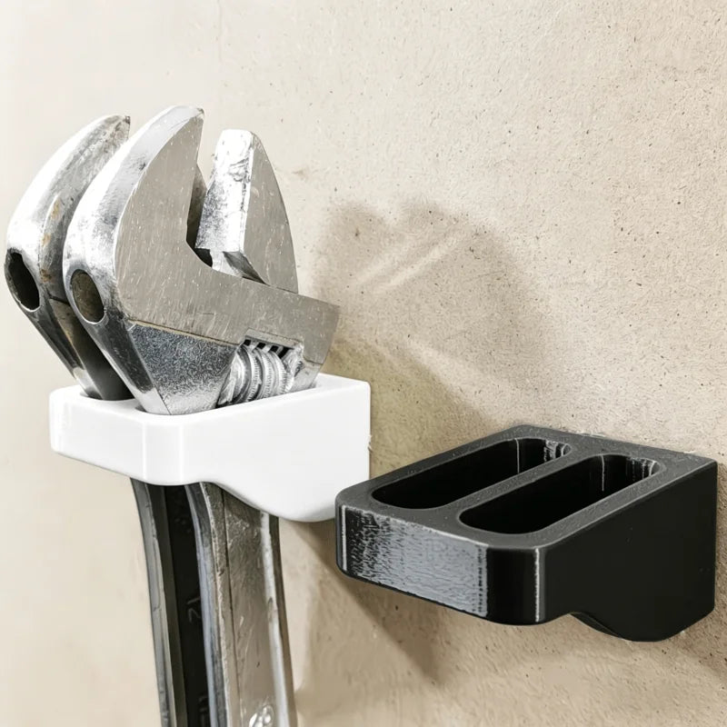 A silver wrench organizer rack with double slots is mounted on a wall, featuring a white holder and a black storage piece.