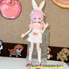 A female doll dressed in a pink maid outfit with white frills and bunny ears stands next to a clear glass display.