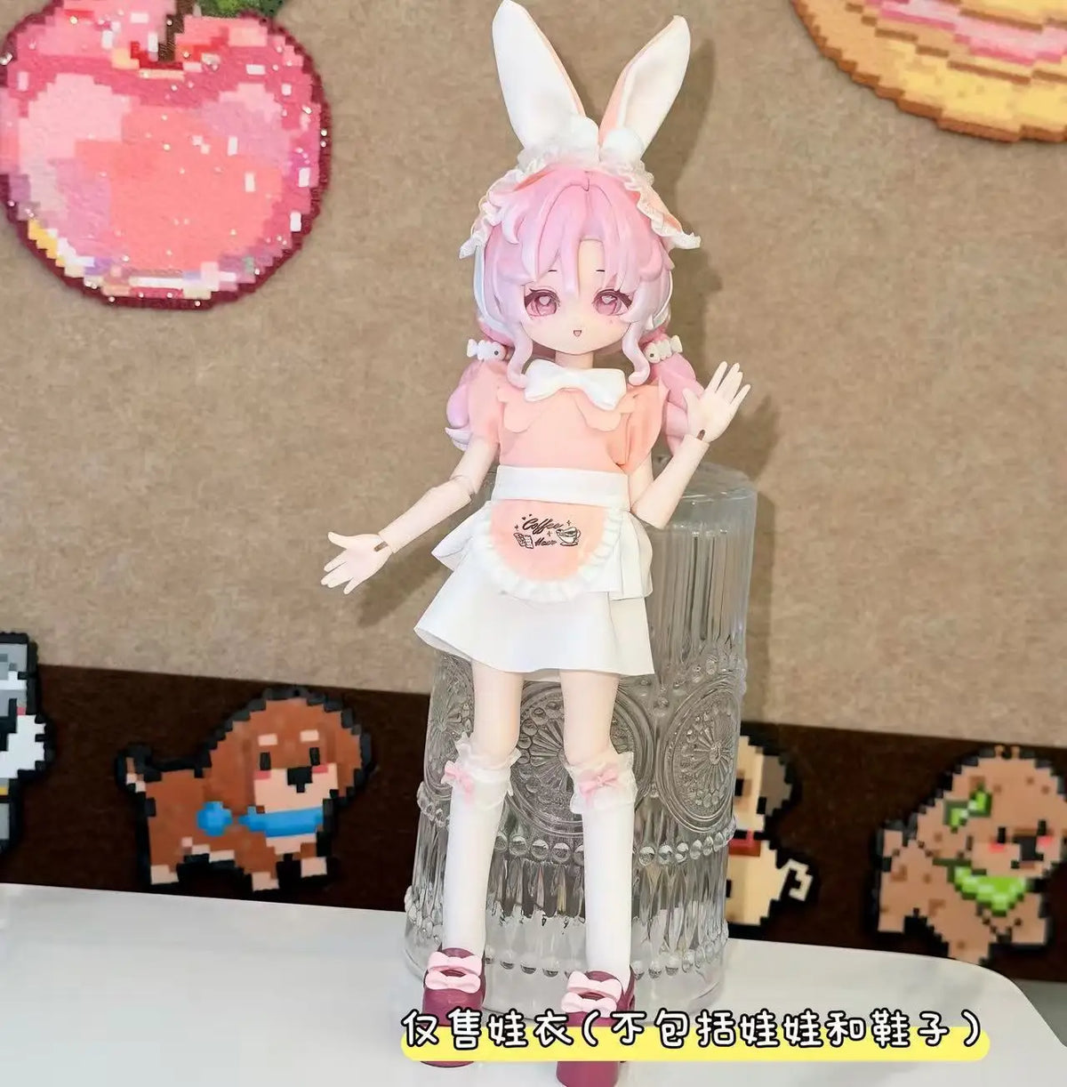 A female doll dressed in a pink maid outfit with white frills and bunny ears stands next to a clear glass display.