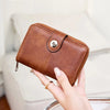 A brown leather wallet with a zipper closure is being held by a hand, demonstrating RFID protection.