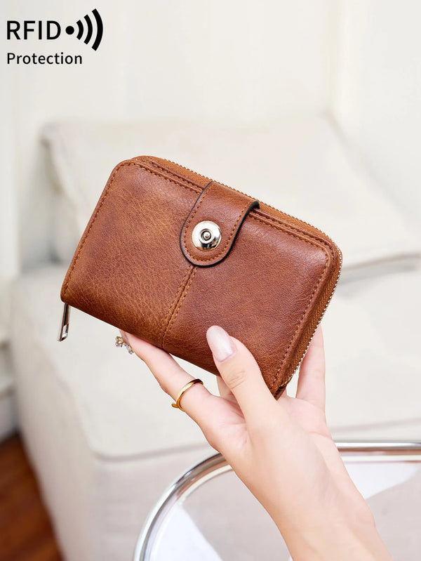 A brown leather wallet with a zipper closure is being held by a hand, demonstrating RFID protection.