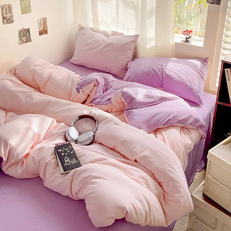 A pink and lavender bedding set featuring a duvet cover, flat sheet, and pillows on a bed.