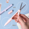 A hand holds a pink folding pen-shaped safety scissors, showing the scissor blades and the pen body.