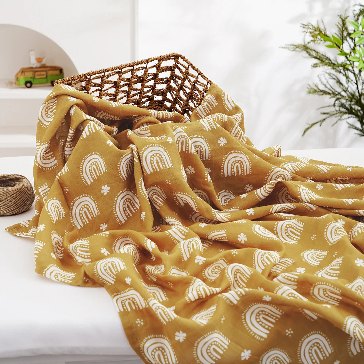 A mustard yellow muslin baby swaddle blanket with white rainbow patterns draped on a white surface.