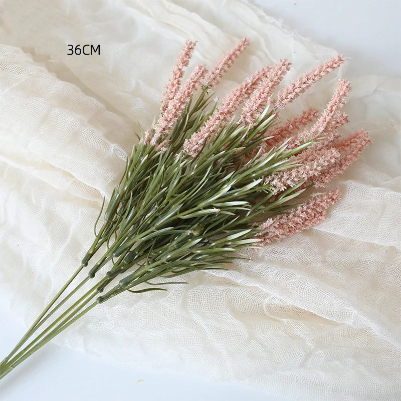 Ein Zweig künstlicher Lavendel mit rosa Blüten und grünen Stielen auf einem hellen Stoff.