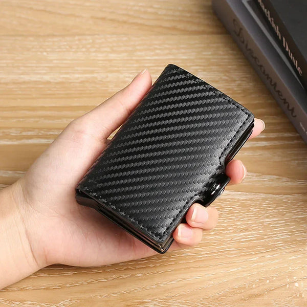 A hand holds a black carbon fiber wallet with a textured pattern on a wooden surface.