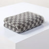 A folded gray and white plaid cotton bath towel set resting on a white surface.