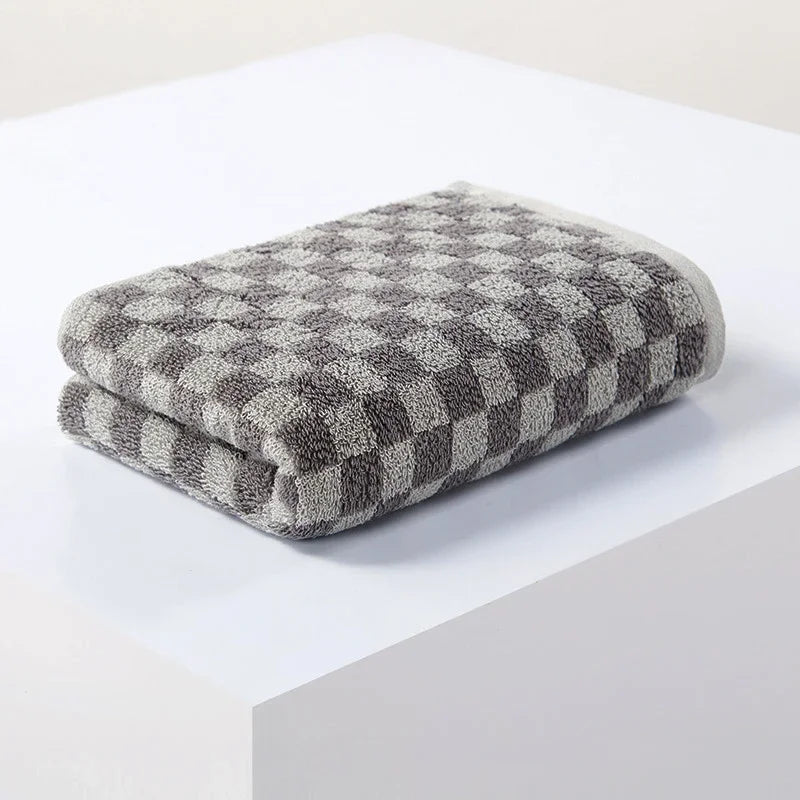 A folded gray and white plaid cotton bath towel set resting on a white surface.