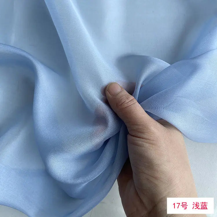 A hand is folding a piece of light blue silk chiffon fabric.