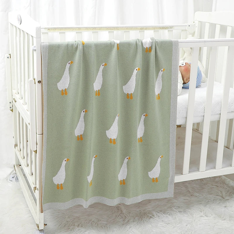 A soft cotton baby swaddle blanket with a light green background featuring a repeating pattern of small white cartoon birds.