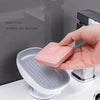 A hand places a pink leaf-shaped suction cup soap dish onto a white bathroom shelf.