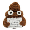 A brown crocheted plush ornament shaped like a creature with large eyes and a white tag that reads Positive POO I may be a ti
