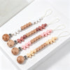 A set of personalized silicone pacifier clips with various floral designs and wooden beads on white lanyards.