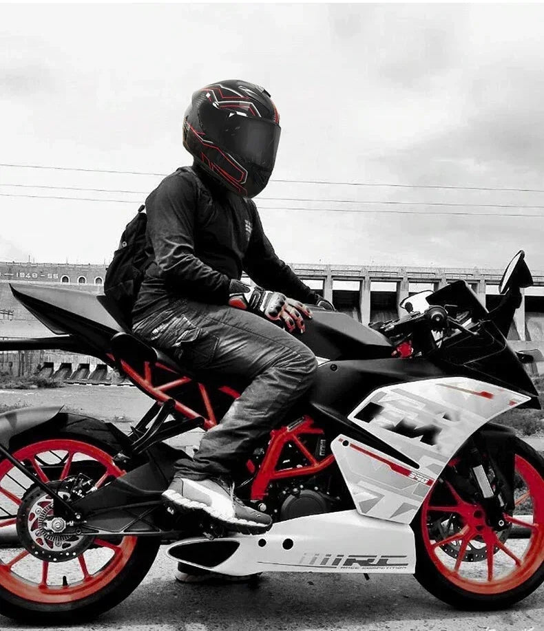 A person wearing a black full face motorcycle helmet is sitting on a black and white sport bike against an overcast sky.