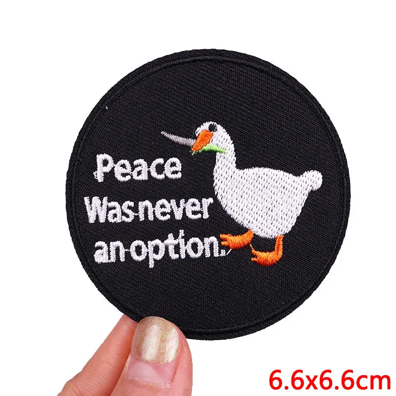 Black embroidered patch featuring a white duck with peace text on it