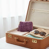 A brown leather jewelry organizer box with an open lid displaying a purple velvet pouch and sunglasses.