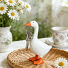A white goose sculpture with an orange beak and legs holding a silver key, displayed on a woven tray.