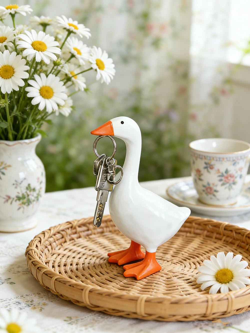 A white goose sculpture with an orange beak and legs holding a silver key, displayed on a woven tray.