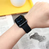 A close-up of a black Apple Watch on a wrist, resting near a yellow surface and newspaper.