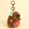 A brown capybara plush toy with a light yellow ear and an orange patterned accessory, attached to a metal keychain.