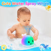 A baby is playing with a light-up whale bath toy that sprays water in a bathtub.