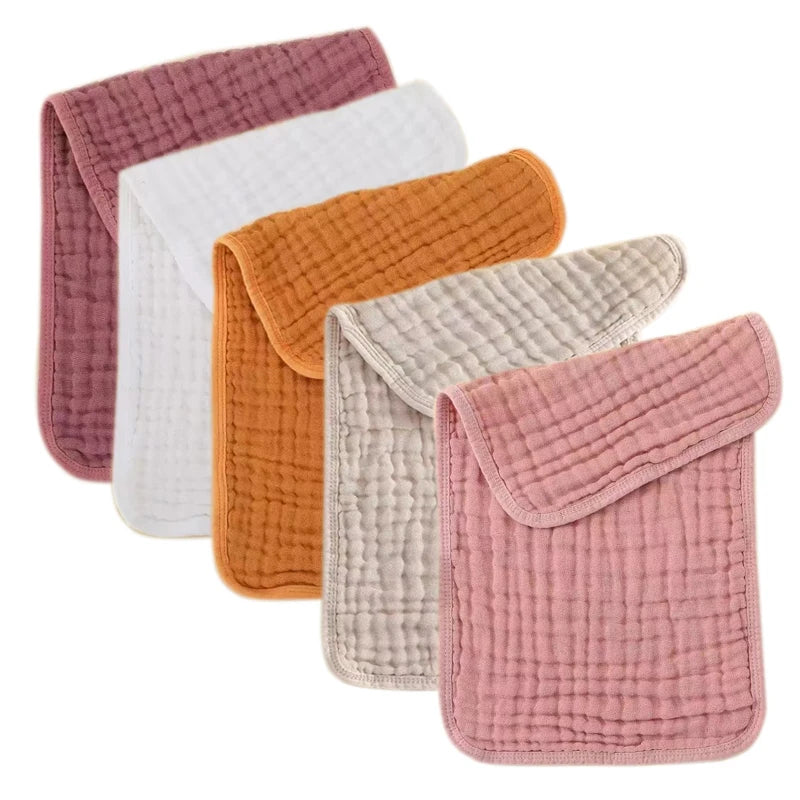 A stack of five colored muslin baby burp cloths in pink, white, orange, and beige.