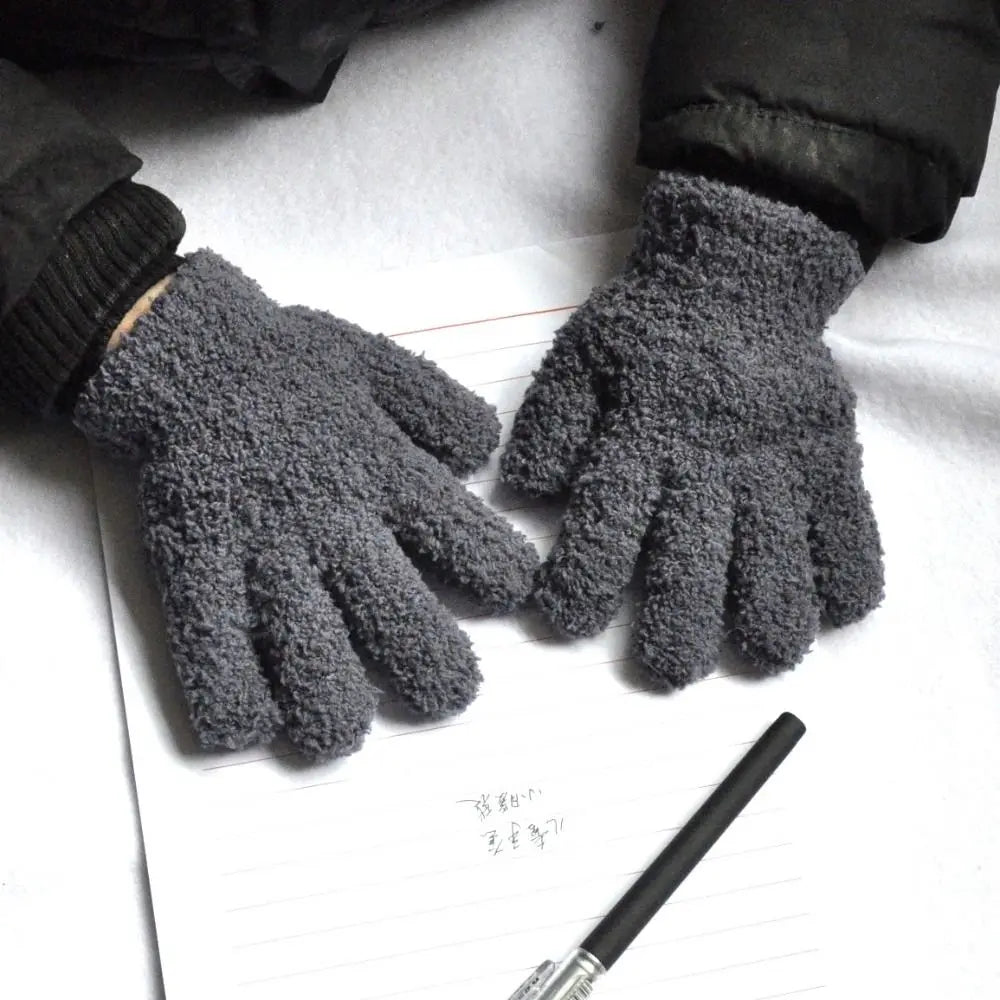 A pair of dark gray, fuzzy plush winter gloves resting on a piece of white paper.