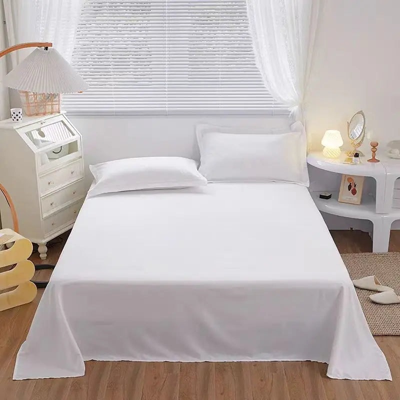 Eine weiße Bettdecke liegt auf einem Bett mit weißen Kissen, neben einem Fenster und Nachttisch.