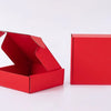 Eine rote Wellpappkartonbox liegt geöffnet neben einer geschlossenen roten Box.