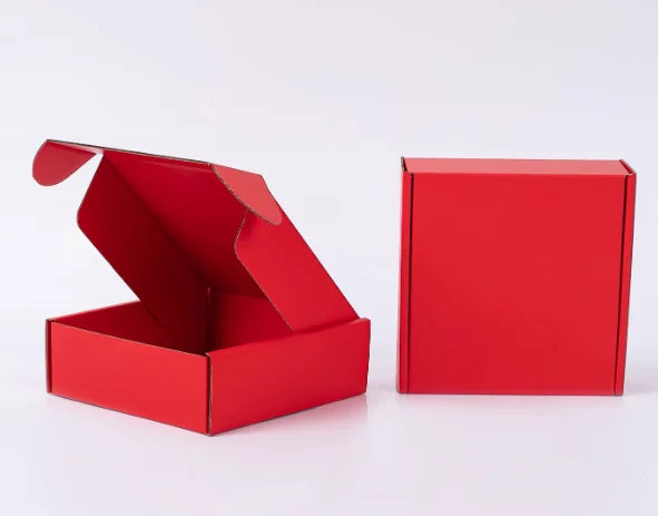 Eine rote Wellpappkartonbox liegt geöffnet neben einer geschlossenen roten Box.