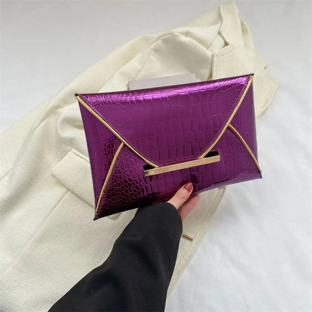 A purple crocodile pattern PU envelope clutch with a gold trim is held against a cream-colored jacket.
