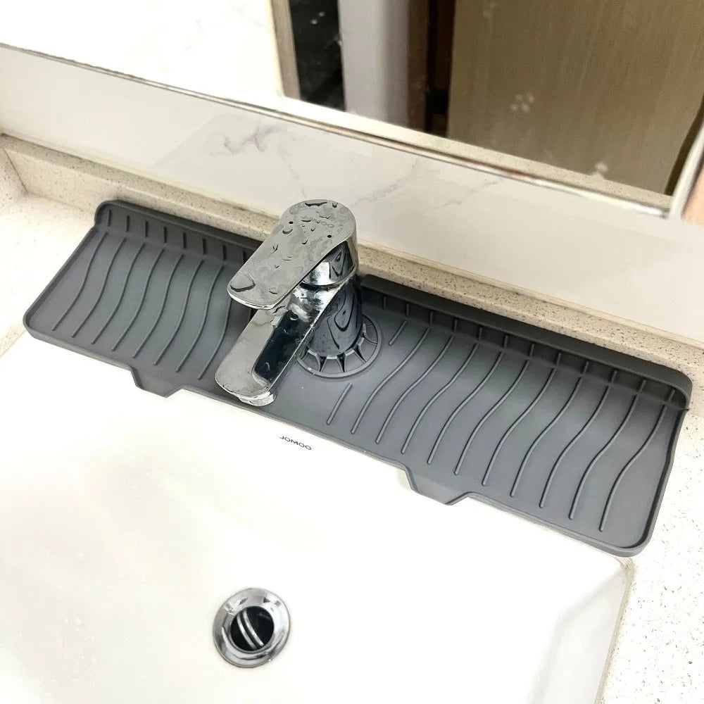 A black silicone faucet splash mat with a metal spout is placed on a white countertop.