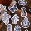 A collection of vintage alchemy washi stickers featuring metal-embossed designs like a flask, key, and clock on a wooden surf