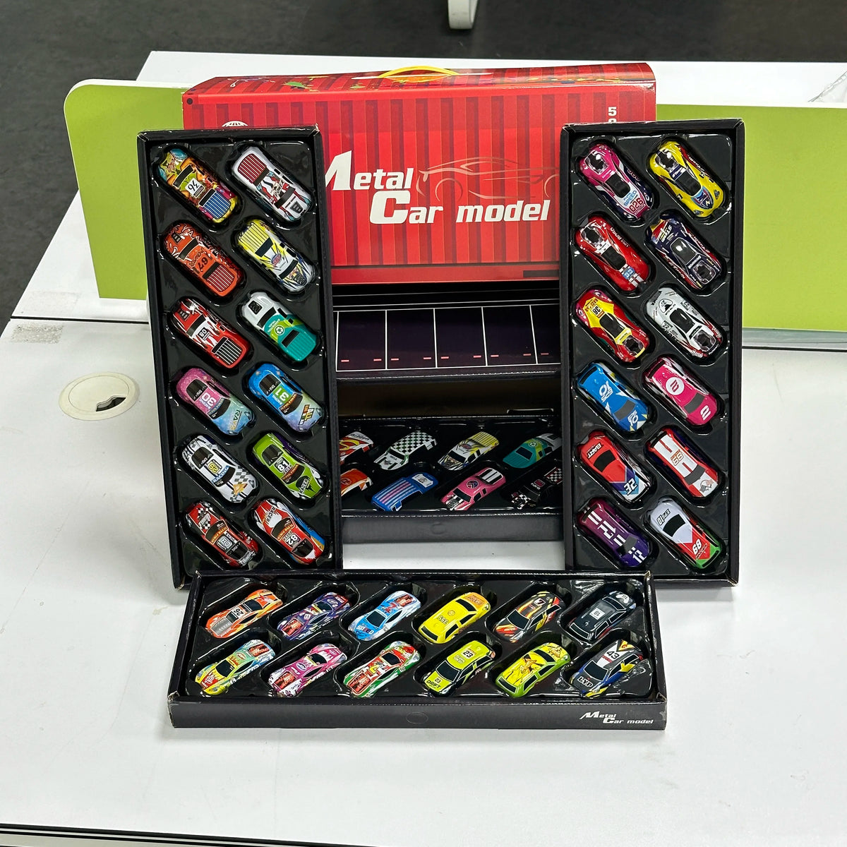 A collection of mini pull-back plastic toy cars in various colors and designs displayed in a black storage box.