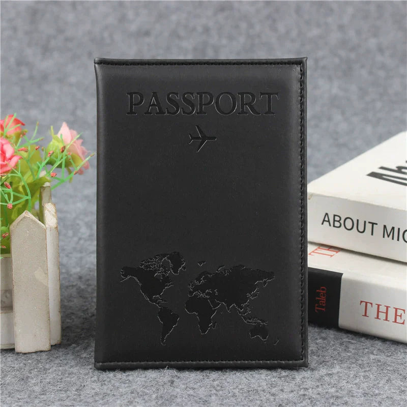 Black leather passport holder with embossed world map design and card slots resting on a gray surface.