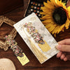 A hand holds a vintage metal bookmark with an artistic hollow design and tassel against a dark wooden background and a sunflo